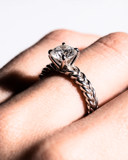 Silver solitaire ring with a clear round stone and braided band, shown on a finger